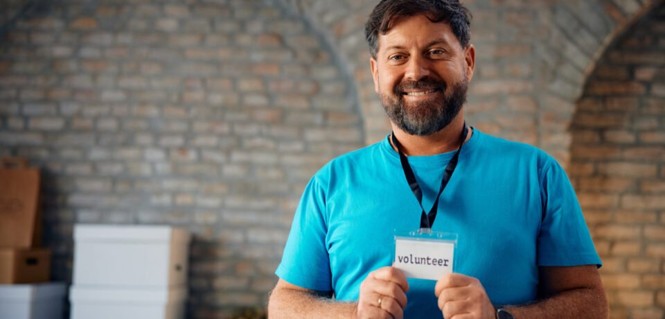 Happy man holding his volunteer identification card and looking at camera. Copy space.