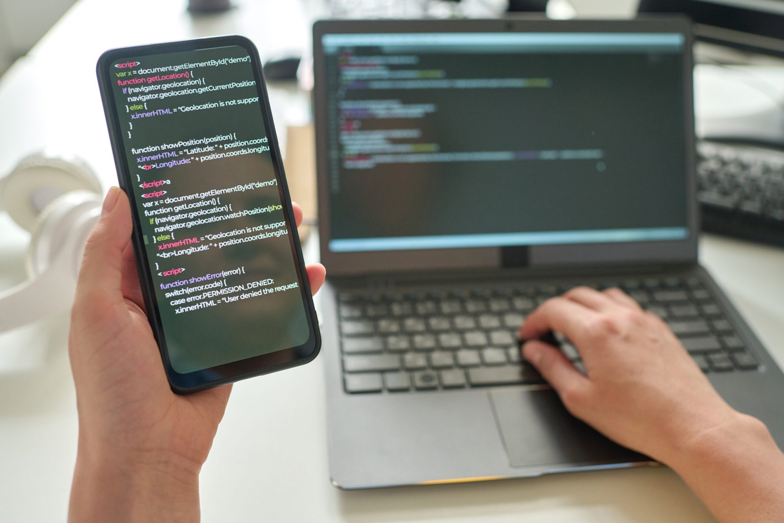 Close-up of programmer holding smartphone with codes in her hands and connecting it with laptop at table