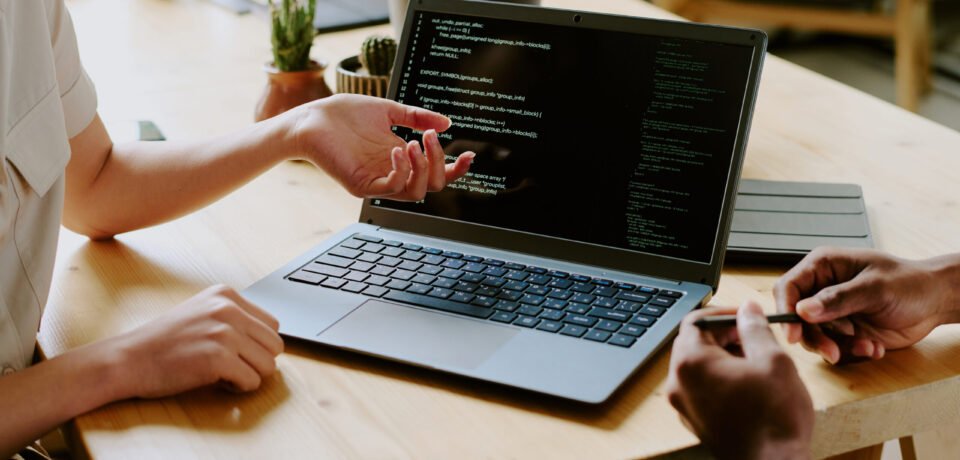 Unrecognizable biracial male and female programmers sitting at wooden desk and working together on code using laptop