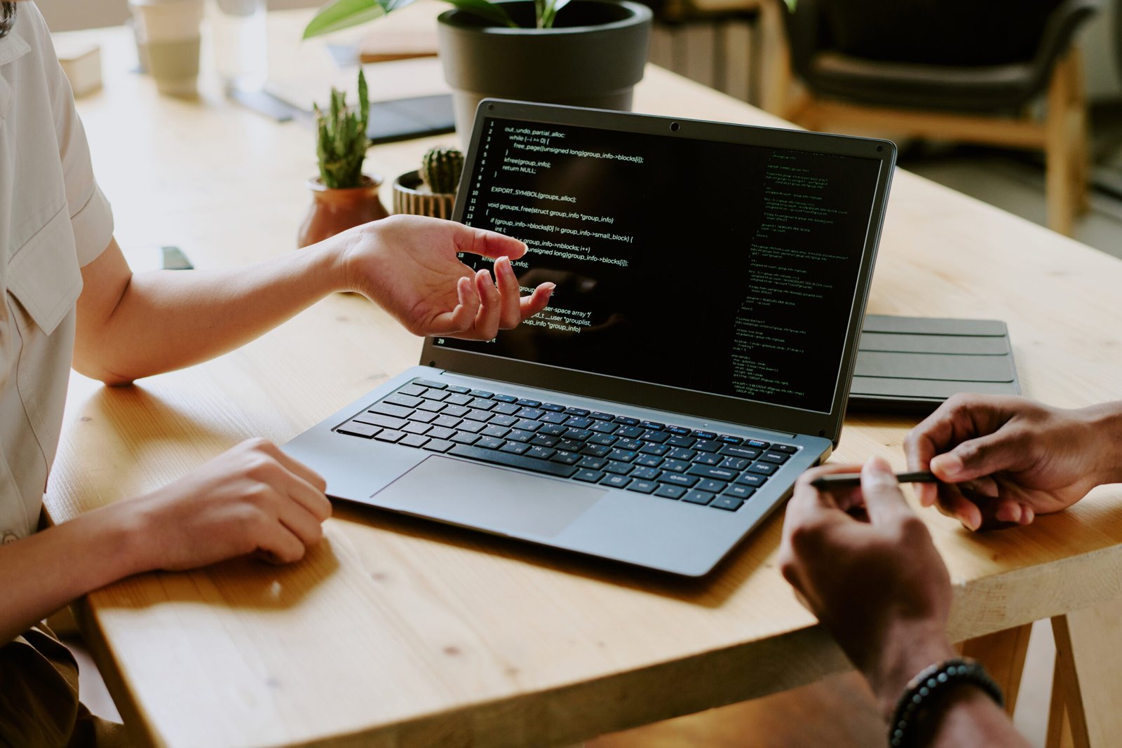 Unrecognizable biracial male and female programmers sitting at wooden desk and working together on code using laptop