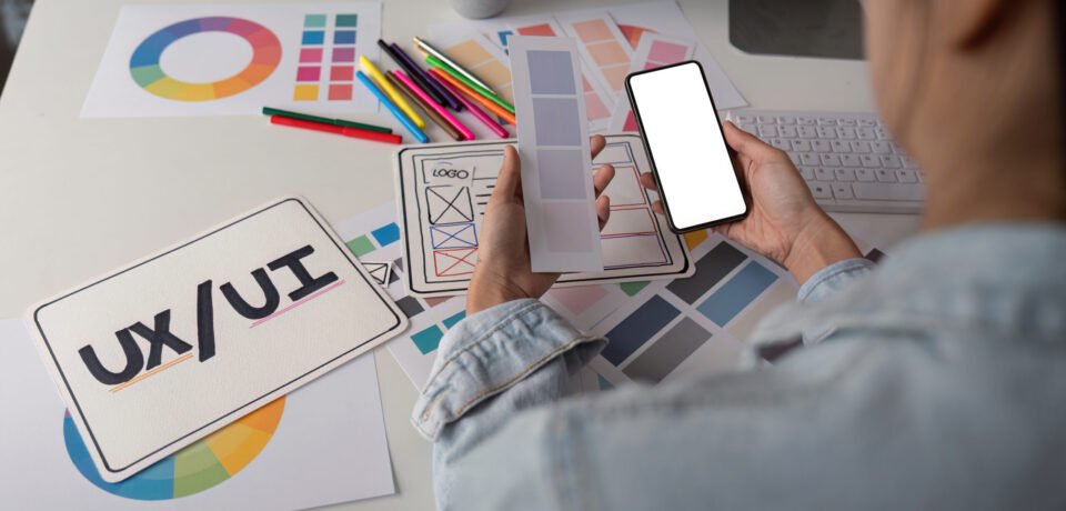 Woman hands holding a smartphone white screen mockup over modern graphic designer office desk.