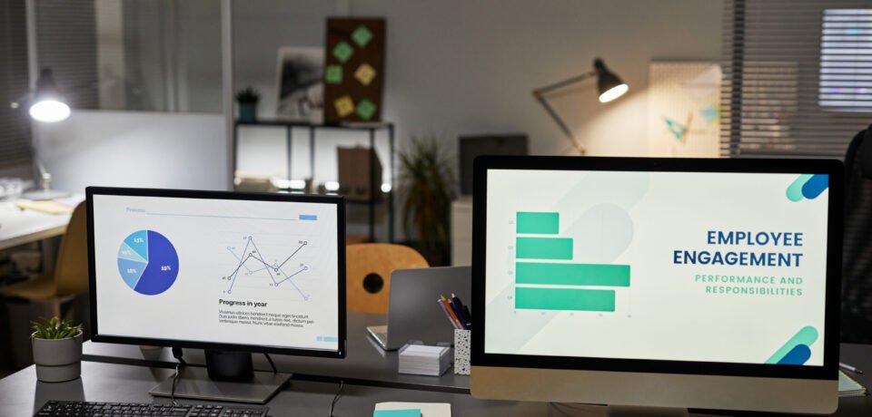 Background image of two computer monitors in office with Employee engagement charts, copy space