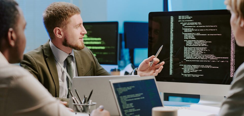 Group of three diverse young cybersecurity specialists discussing issues during meeting in office equipped with modern computers