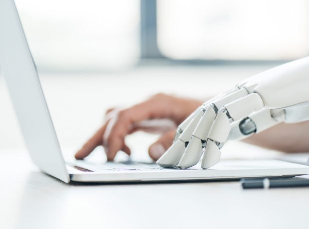 selective focus of human and robot hands typing on laptop at workplace