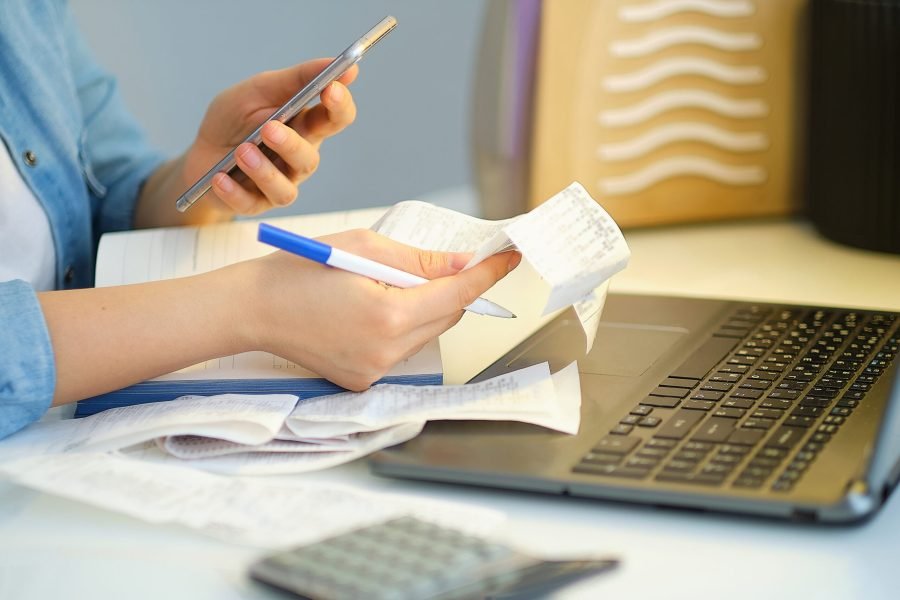 woman using a pen writing on bank account book while holding the bills to calculate in living room at home. Expenses, account, taxes, home budget concept
